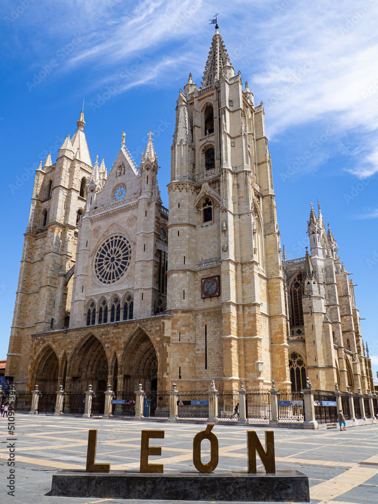 Majestuosa fachada con figuras de la catedral de León, en España., de estilo gótico, con torres , arcos cristales, elevándose sobre el cielo con nubes blancas, en verano de 2021