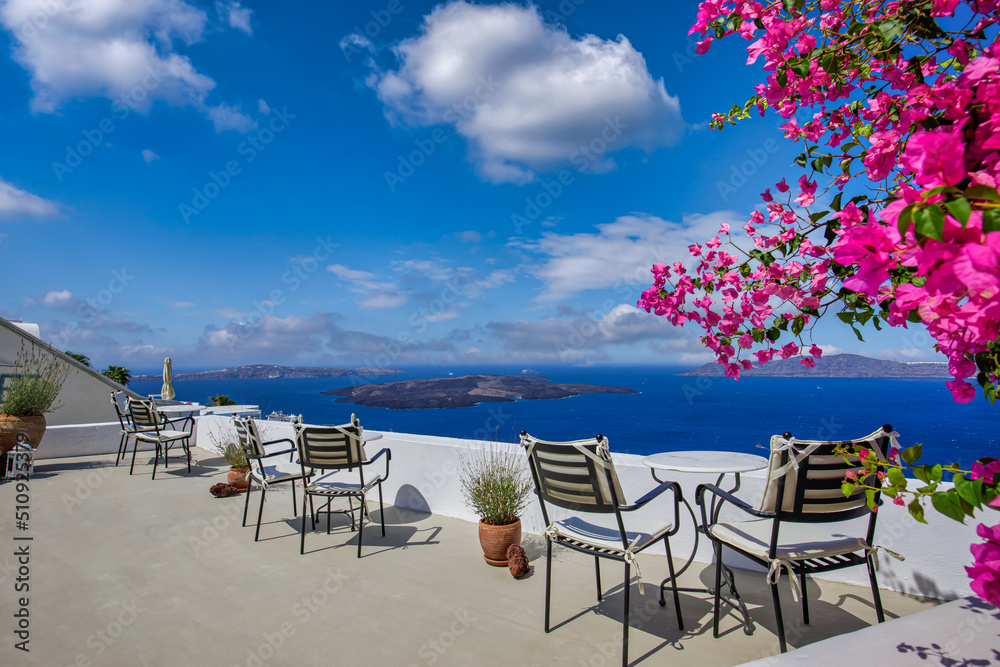 Romantic couple outdoor white marble tables chairs on terrace with flowers overlooking sea, Oia Village, Santorini, Cyclades, Greece. Summer holiday, idyllic vacation. Panoramic travel landscape
