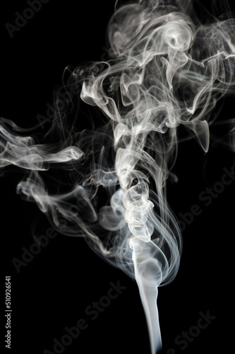 Fototapeta Naklejka Na Ścianę i Meble -  Puffs and curls of white smoke against a black background rising from a burning stick