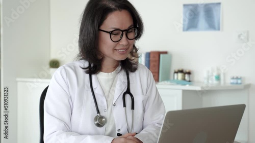 Asian ethnicity female doctor wears white coat. Doctor talking to patient with video call app on laptop. Distance consultation. Telemedicine, Remote. Healthcare services concept. 4k footage