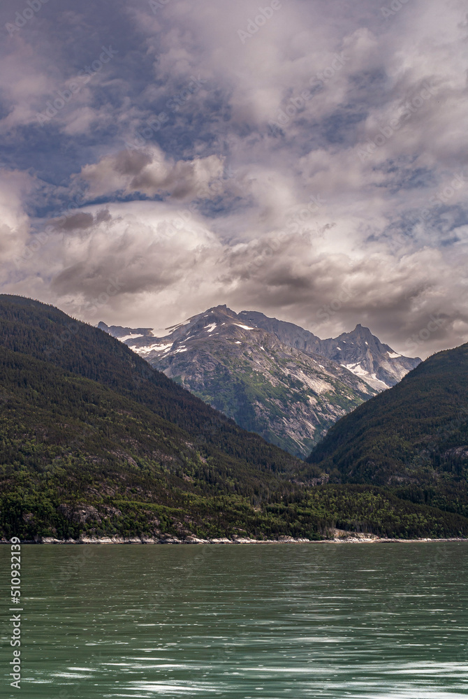 Skagway, Alaska, USA - July 20, 2011: Taiya Inlet above Chilkoot Inlet. Portrait of fjord, forested mountains descend into green ocean water. Snow covered tops on horizon, all under blue cloudscape.