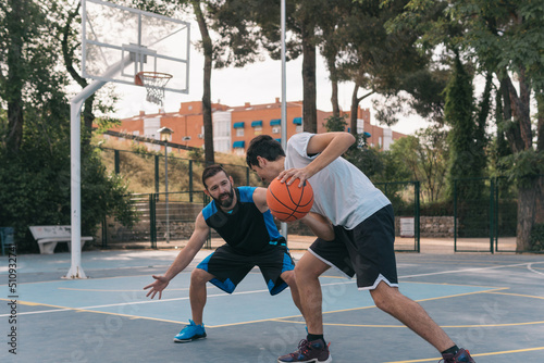 Young sporty boy trying to dribble past his opponent while he defends without the ball. Street basketball game on a blue court between two friends and rivals on the field. © Jorge
