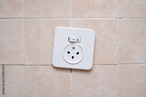 Crookedly mounted electrical socket with switch. On ceramic tile in Israel