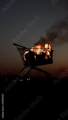 A shopping cart is burning In an abandoned area against the background of a golden sunset and night, slow motion. vertical video
