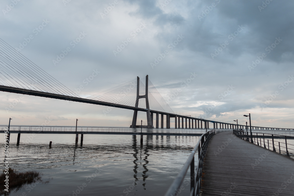 Beautiful long bridge with a wooden pier and the sea against a cloudy sky. Vasco da Gama Bridge in Lisbon