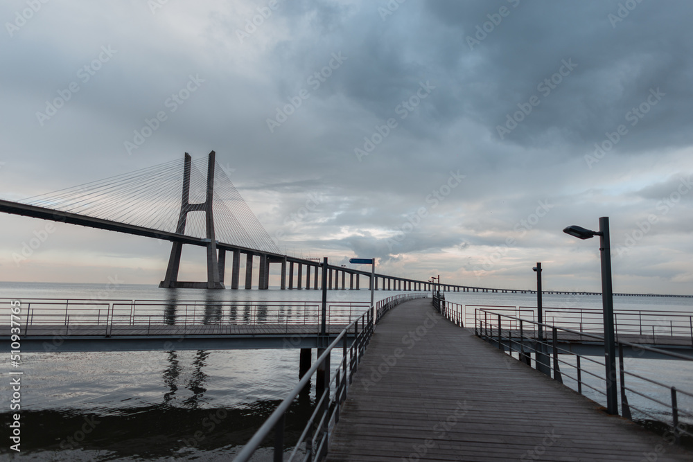 Beautiful wooden pier and Vasque Dagama bridge with clouds in Lisbon, Portugal