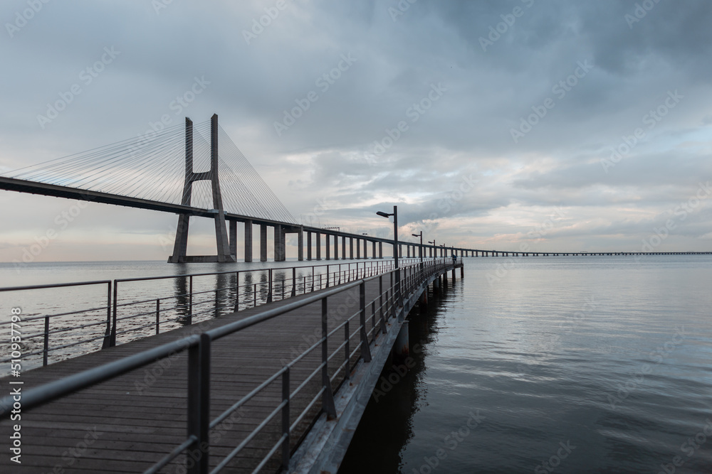 Amazing bridge and wooden pier on a gray sky with clouds. Lisbon, Portugal Amazing bridge and wooden pier on a gray sky with clouds. Lisbon, Portugal