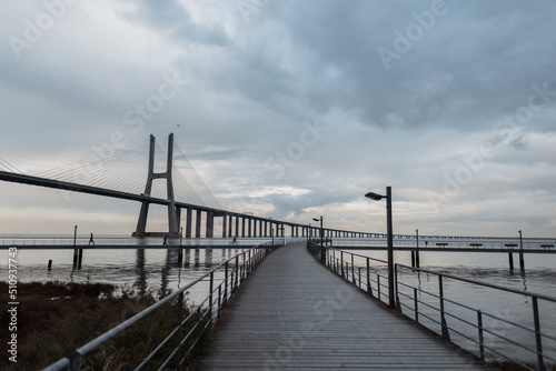 Beautiful view of the wooden pier, the long Vasque da Gama Bridge in cloudy weather. Journey to Lisbon, Portugal © alones
