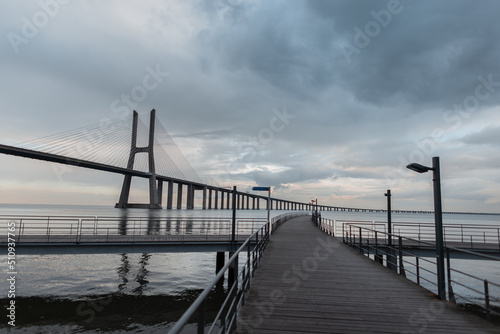 Beautiful wooden pier and Vasque Dagama bridge with clouds in Lisbon  Portugal