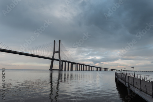 Amazing beautiful long Vasque Dagama Bridge with its pier and gray clouds in Lisbon, Portugal © alones