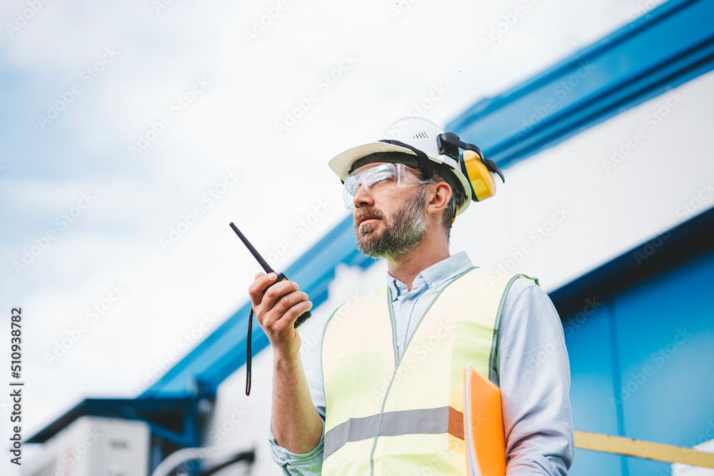 Portrait of engineer using walkie-talkie talking in production site. Bearded man worker control produce process Portrait of engineer using walkie-talkie talking in production site. Bearded man worker control produce process