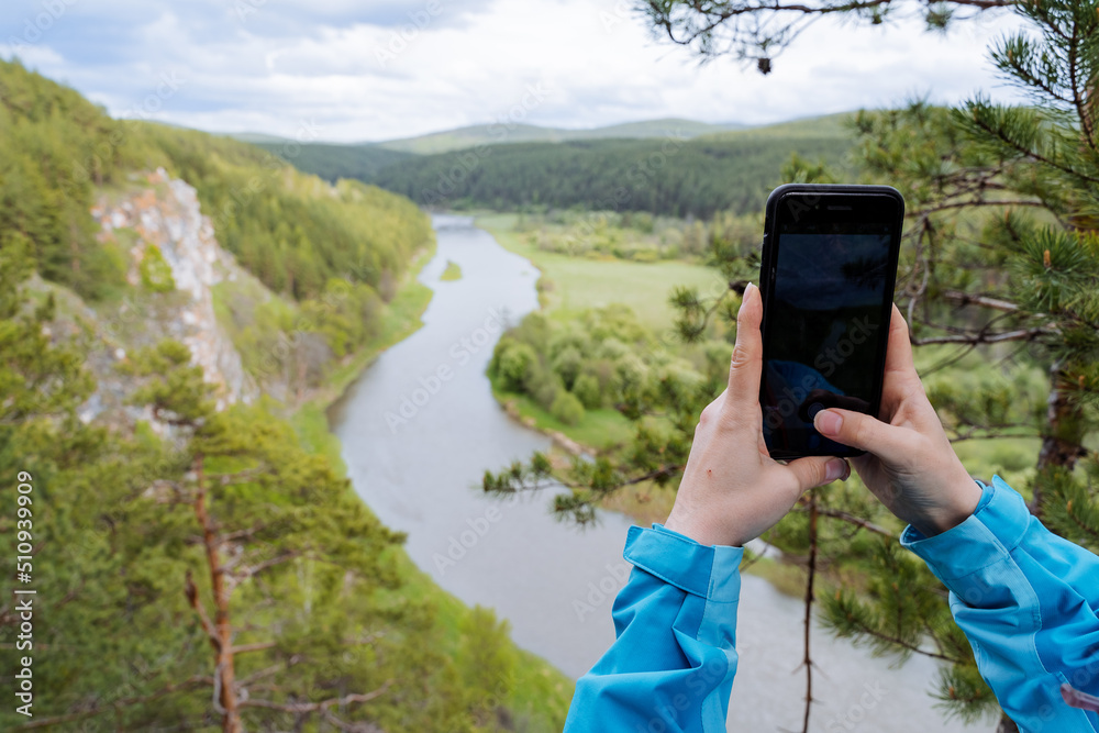 A person photographs a landscape on a phone, women's hands hold a smartphone while taking a selfie, beautiful nature in a cell phone lens.