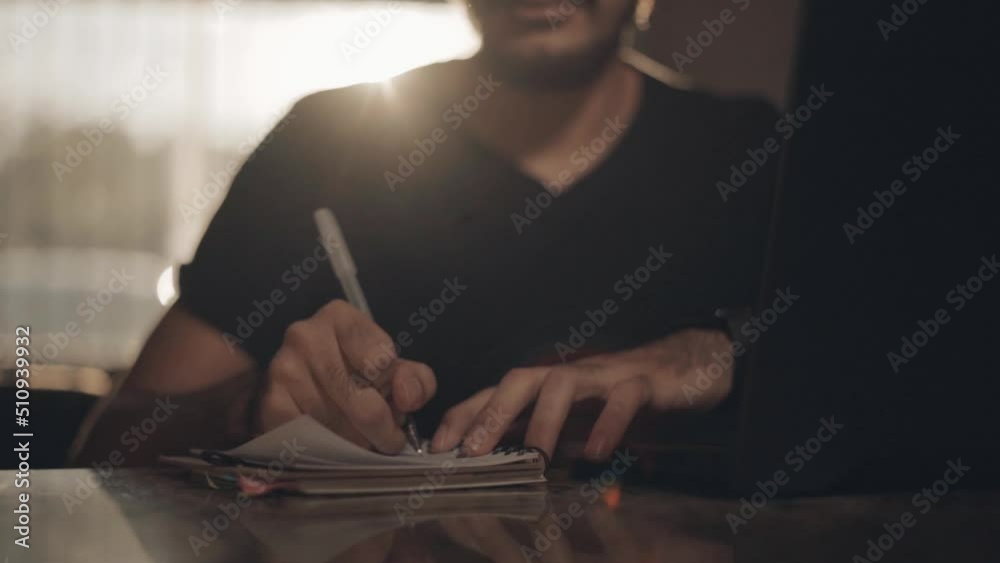 Man writing a book. Bright young man taking college classes at home. Business person jotting down innovative ideas and mapping out goals and objectives for his venture