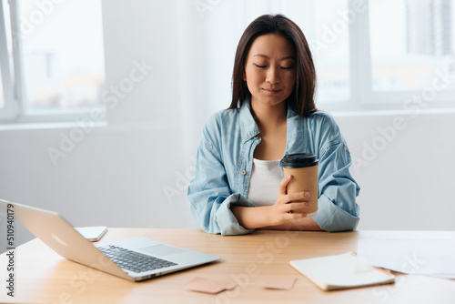 Happy smiling pensive young Asian cute businesswoman hold coffee cup enjoy looks aside in light office interior. Freelancer work at home. Lady corporation leader concept. Copy space Offer