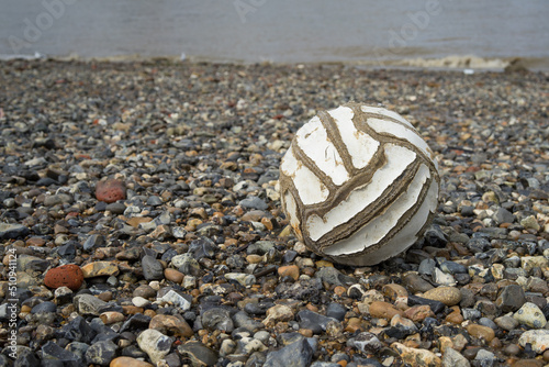 Old football washed up on a stony beach photo