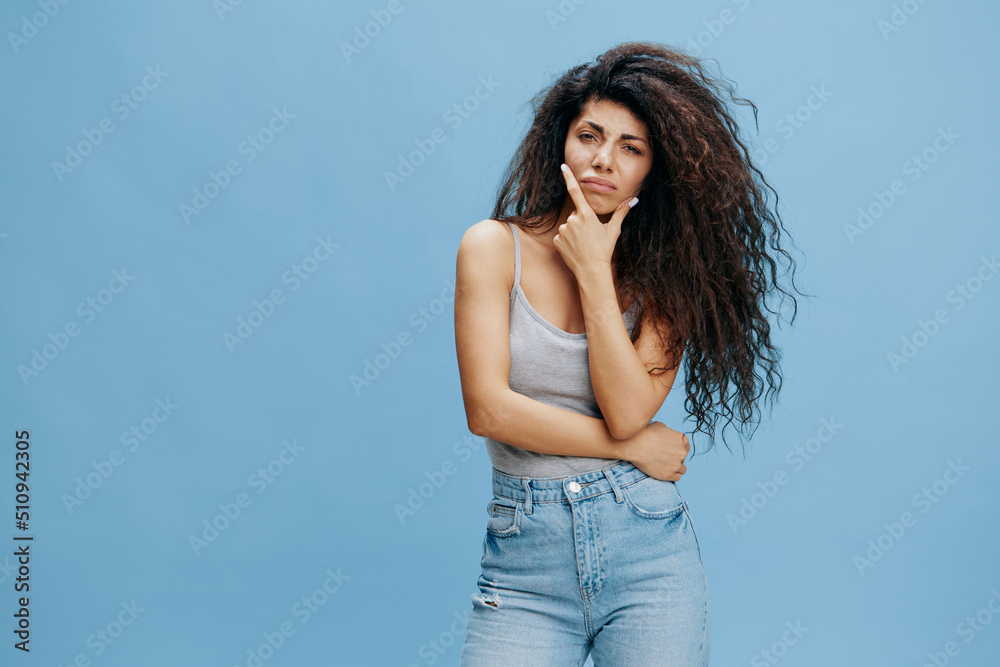 Thoughtful beautiful Latin female with afro with hand near cheek, look at camera. Fashion. Studio shoot over blue sky background. Copy space, free place for design ad Thoughtful beautiful Latin female with afro with hand near cheek, look at camera. Fashion. Studio shoot over blue sky background. Copy space, free place for design ad