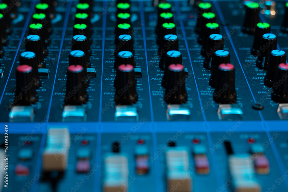 An analogue sound mixing desk glowing in a blue light An analogue sound mixing desk glowing in a blue light