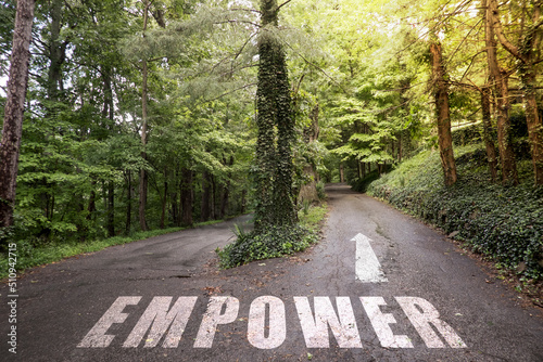 The text Empower on a road in the woods with sun rays shining.
