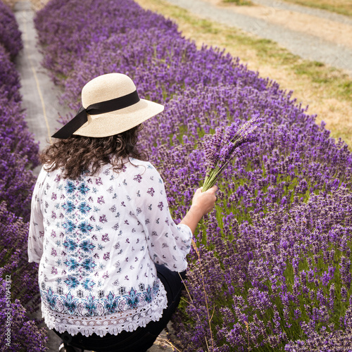 Woman with Dark Curly Hair and Sun Hat Holding Bouquet of Purple Lavender in Lavender Field