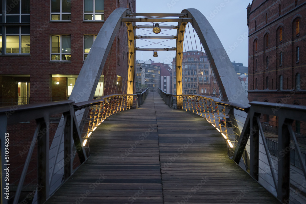 Metal and wooden industrial pedestrian bridge in the old industrial area of Hamburg in the evening with lights on the metal structure. Hamburg, Germany