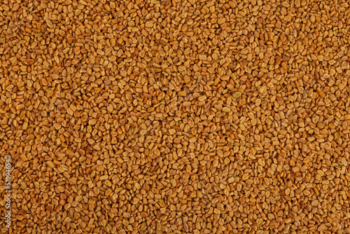 Texture of yellow fenugreek seeds or shambhala, helba seeds as food background. Fenugreek is traditional Indian seasoning. Top view, close-up photo