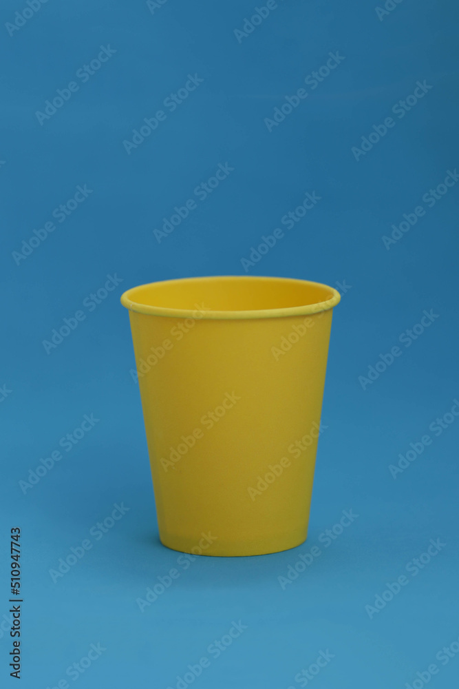 Takeaway disposable yellow paper cup on a blue background, isolated object, photo with copy space.  Mock-up for the logo,  side view. Ukrainian national colors