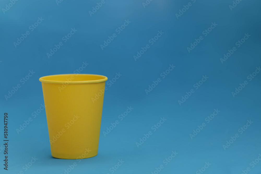 Takeaway disposable yellow paper cup on a blue background, isolated object, photo with copy space. Mock-up for the logo, side view. Ukrainian national colors Takeaway disposable yellow paper cup on a blue background, isolated object, photo with copy space. Mock-up for the logo, side view. Ukrainian national colors