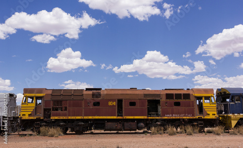 An old train sitting in a yard with a cloudy blue sky behind