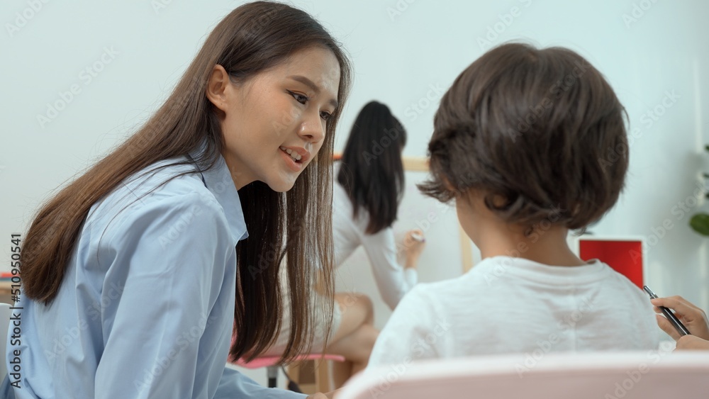 Asian female teacher teach and write on whiteboard while children sit on the chair in classroom, Multi-ethnic preschool teacher and students in classroom. Kindergarten pre school concept. Asian female teacher teach and write on whiteboard while children sit on the chair in classroom, Multi-ethnic preschool teacher and students in classroom. Kindergarten pre school concept.