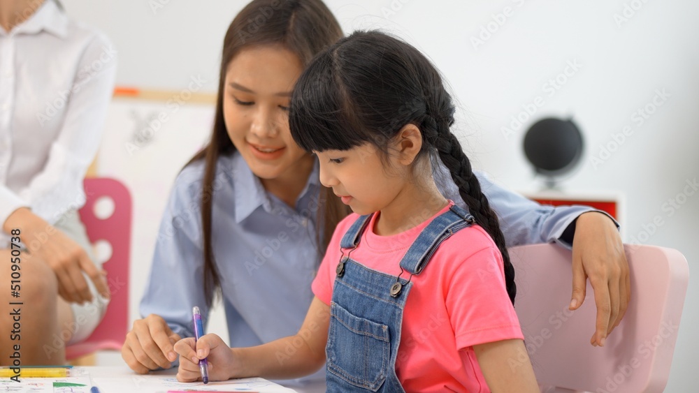 Obraz premium Asian little girl finish paint color book on the table and high five with teacher in classroom,Multi-ethnic preschool young asian teacher and students in classroom.Kindergarten and study concept.