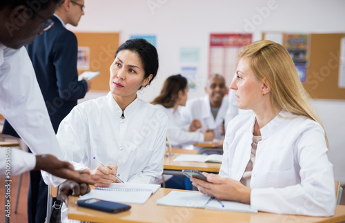 Adult people in white lab coats working in small groups during professional training course, discussing task set by teacher