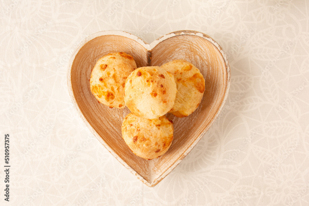 Cheese bread (Brazilian pao de queijo mineiro), top view, white background, on a heart shaped plate.