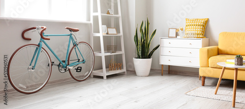 Stylish interior of room with bicycle, shelves, chest of drawers and armchair