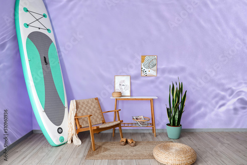 Photography Interior of room with armchair, table and board for sup surfing near wall with p