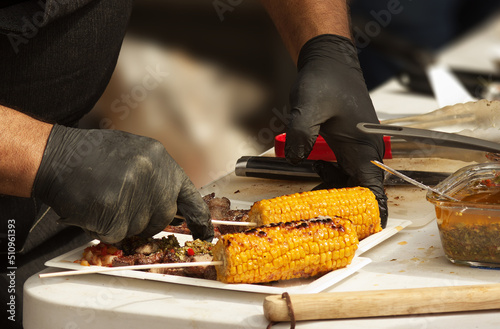 Chef serves portions of grilled meat and corn on the cob photo