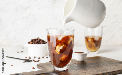 Milk pouring into glass with cold brew coffee on light background