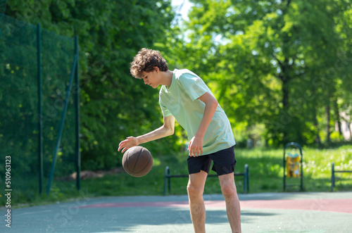 Cute young teenager in green t shirt with a ball plays basketball on court. Sports, hobby, active lifestyle for boys © Natali
