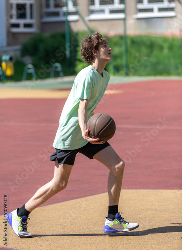 Cute young teenager in green t shirt with a ball plays basketball on court. Sports, hobby, active lifestyle for boys © Natali