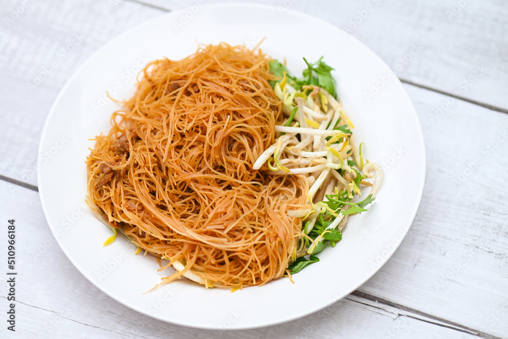 fried noodles vermicelli on white plate , Chinese styled fried noodle with bean sprout and coriander on wooden table - Thai food fried noodles vermicelli on white plate , Chinese styled fried noodle with bean sprout and coriander on wooden table - Thai food