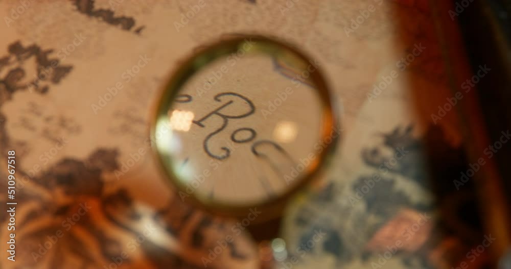 Person carefully examines an ancient map with a magnifying glass, trying to find the place where the treasure chest is buried, close up, top view. Finding the right route Person carefully examines an ancient map with a magnifying glass, trying to find the place where the treasure chest is buried, close up, top view. Finding the right route