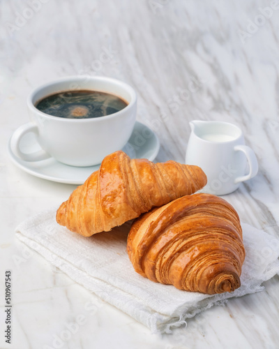 Fresh croissants bread and a cup of coffee on marble table. French breakfast.