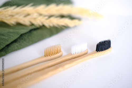 Three bamboo toothbrushes on a green towel with a plant on the background