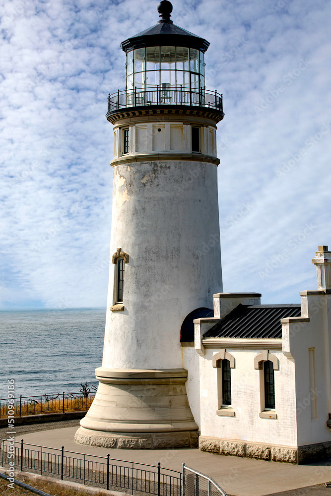North Head Lighthouse against white clouds and bright blue sky on a beautiful sunny afternoon in the Pacific Northwest.
