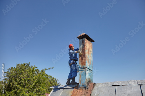 Wallpaper Mural An employee of the Industrial Mountaineering Service paints the chimney on the roof with a spray gun. Professional climber in uniform, helmet and with seat belts. Risky work. Extreme activity. Torontodigital.ca