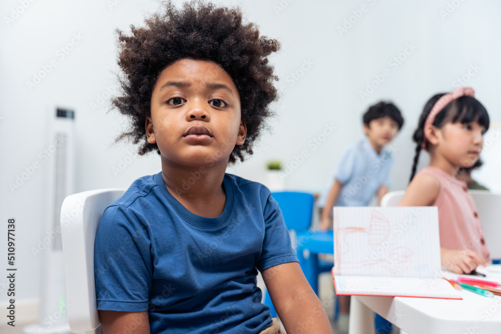 Fototapeta premium Portrait of Stressed African black child boy sitting in classroom. 