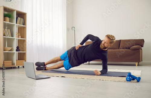 Fit young Caucasian man in sportswear train exercise online on computer at home on lockdown. Toned sporty male have distant workout on laptop with webcam coach lesson. Sport, activity concept.