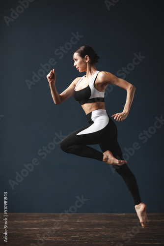 Beautiful athletic woman in black and white sportswear in a jump, posing.