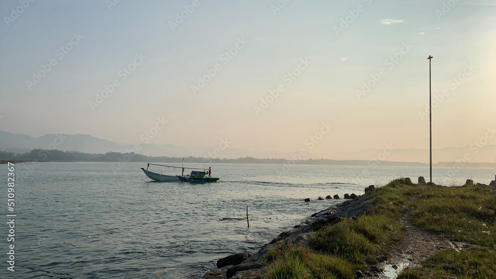 Early morning sea view with sunrise and traditional fishing boats speeding past the pole at the end of the pier