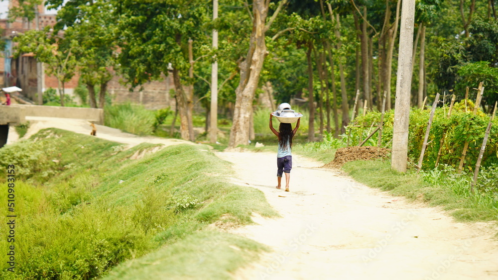 Fototapeta premium An unidentified village little girl is carrying home utensils after washing .