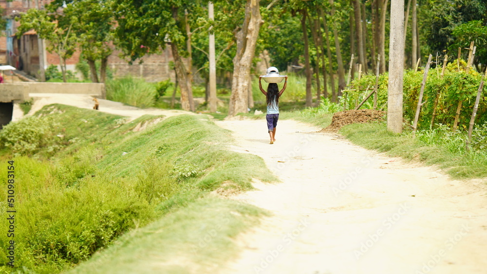 Fototapeta premium An unidentified village little girl is carrying home utensils after washing .